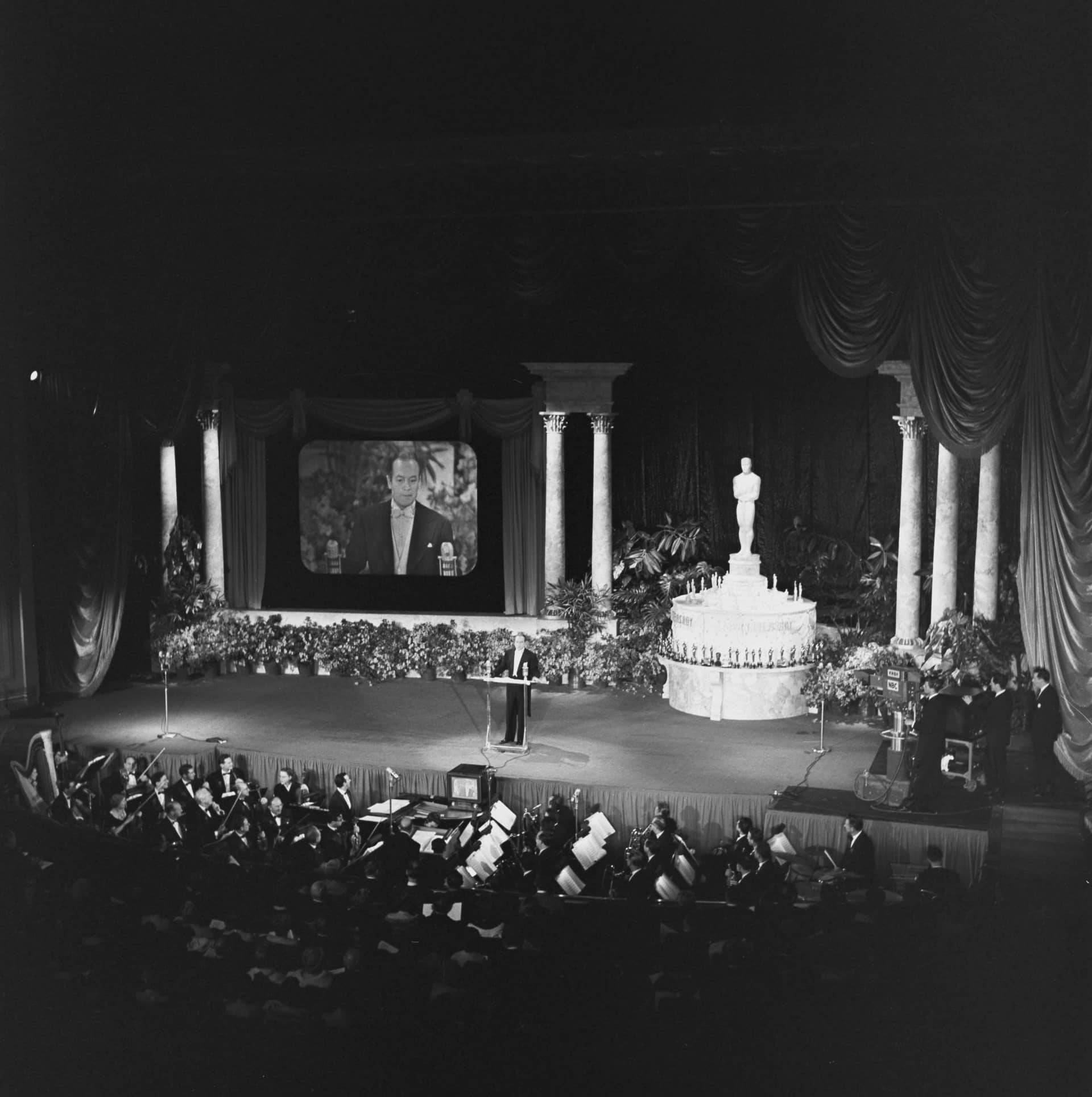 Master of ceremonies Bob Hope in front of the audience at the RKO Pantages Theatre during the 1952 Academy Awards, the first televised ceremony, evidenced by the NBC camera and simulcast screen visible on stage
Courtesy of Academy Awards show photographs, Margaret Herrick Library, Academy of Motion Picture Arts and Sciences
